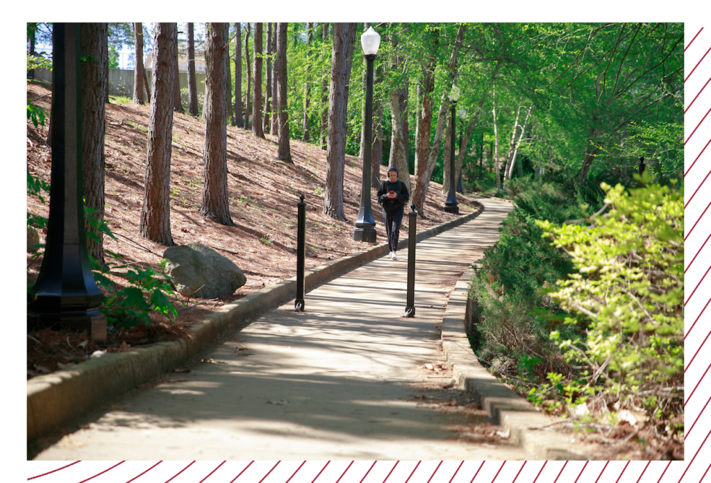 a student walk down the tree-lined path of the riverwalk.