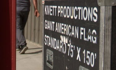 A man walks by a production crate labelled, "KINETT PRODUCTIONS - GIANT AMERICAN FLAG - STANDARD 75 x 150."