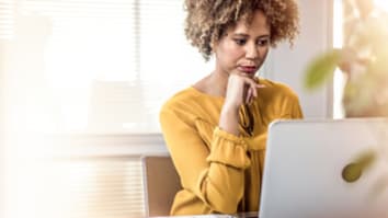 Mixed race woman sitting at a table in an office working on her laptop
