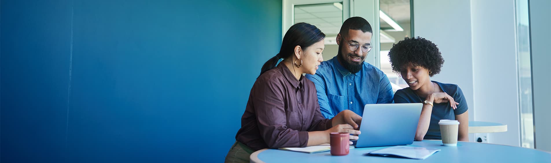 A diverse trio of young office workers huddle around a laptop.