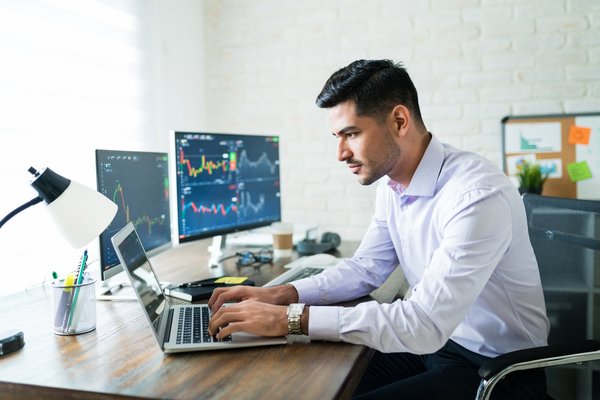 Person looking at stock charts on multiple screens.