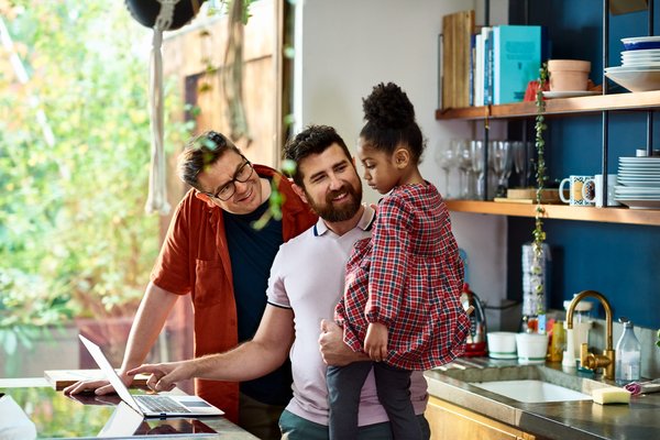 Two adults and a child with a laptop in a kitchen.