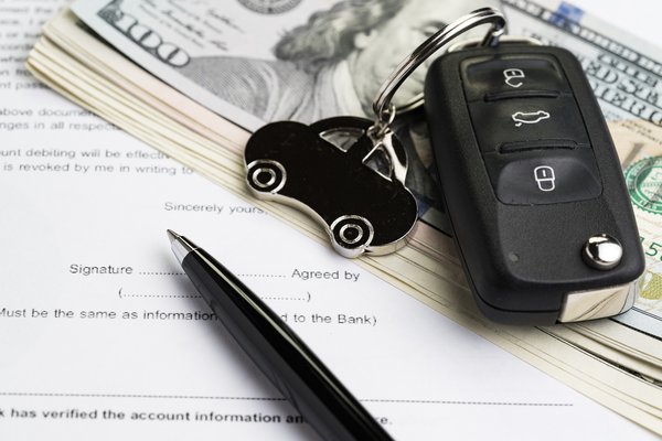 A car key fob, pen, and neat stack of hundred dollar bills on top of auto loan application.