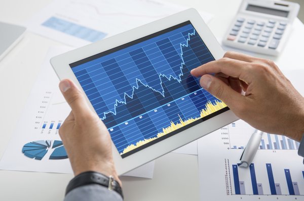 A person analyzing a volatile, but rising, stock chart on a tablet.