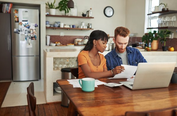 A couple sitting at a table looking at documents and a laptop.