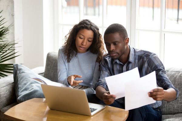 Two people talk about paperwork in front of laptop.