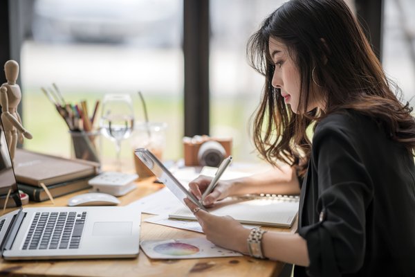 Designer looking at a tablet while writing a note.