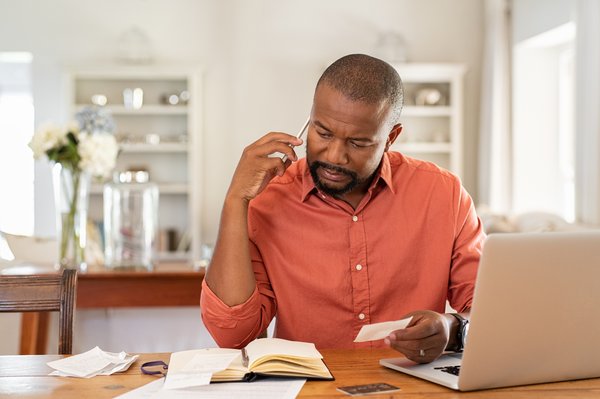 Person on phone looking at books and receipts in front of laptop.