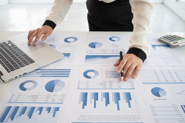 Person working at desk with printed charts and a laptop on top.