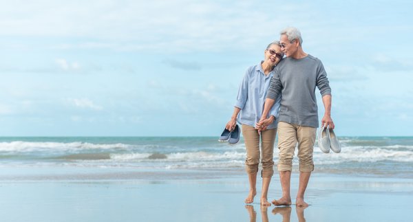 Two people hold hands while walking on the beach.