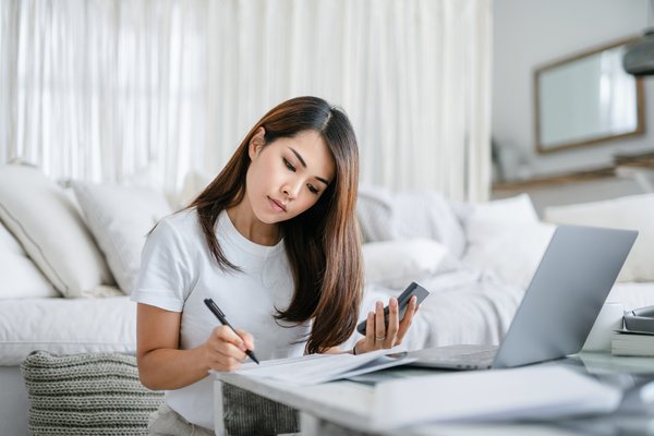 Person taking notes while using phone and laptop.