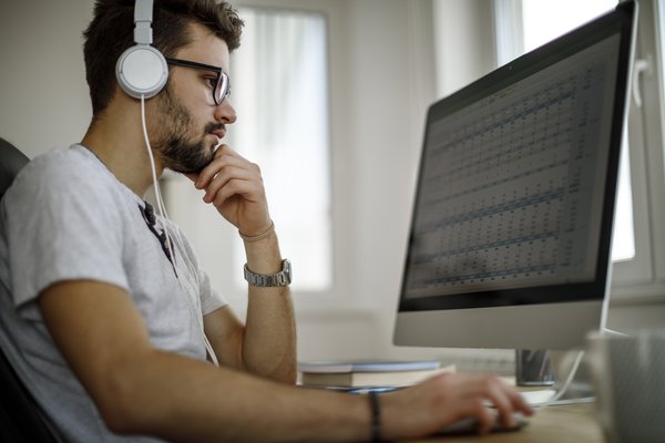 Person wearing headphones while looking at spreadsheet on computer screen.