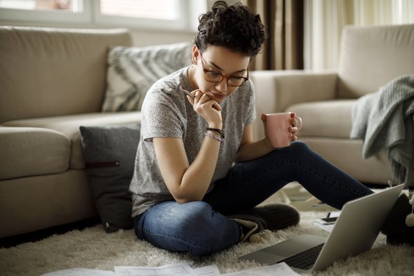 Person sitting on floor looking at documents and laptop.