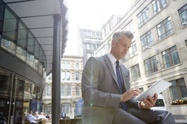 Businessperson sitting outside in city is looking at tablet.