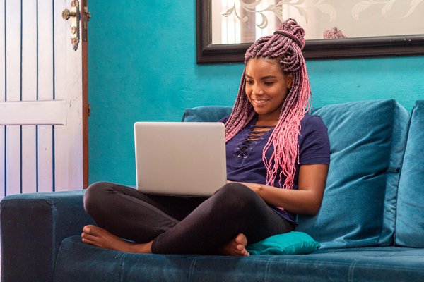 Smiling person sitting cross-legged on couch and using laptop.