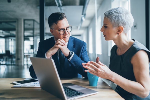 Two businesspeople talking in front of a laptop.