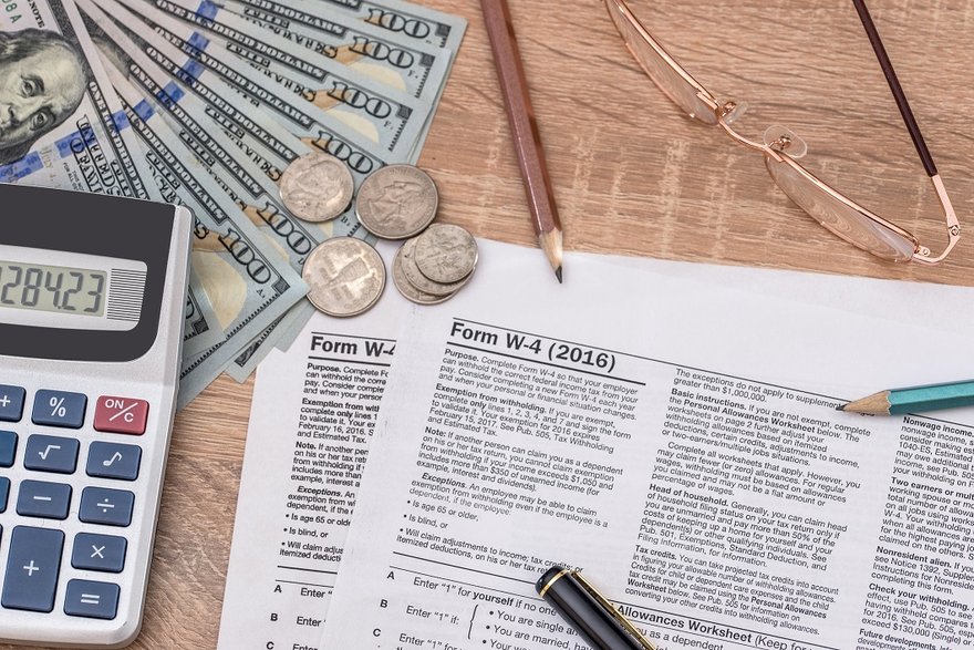 Tax forms with cash, calculator, glasses, and pencils.