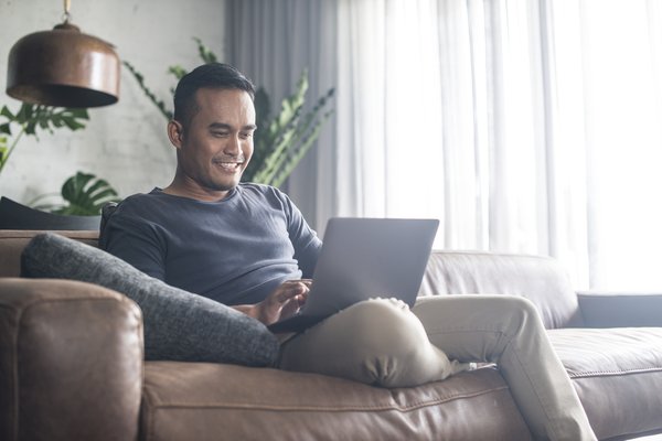 A person sits with a laptop on a couch.