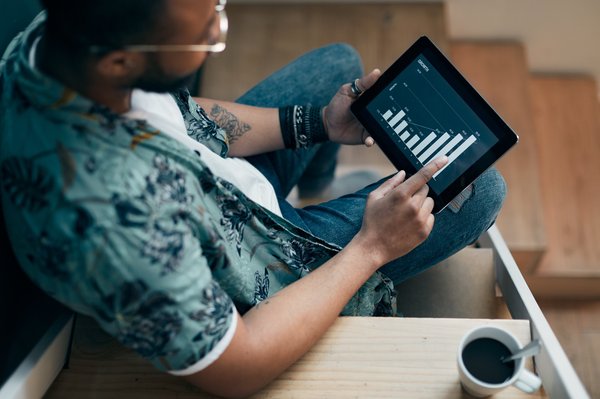 Person uses tablet to view crypto chart while enjoying coffee.