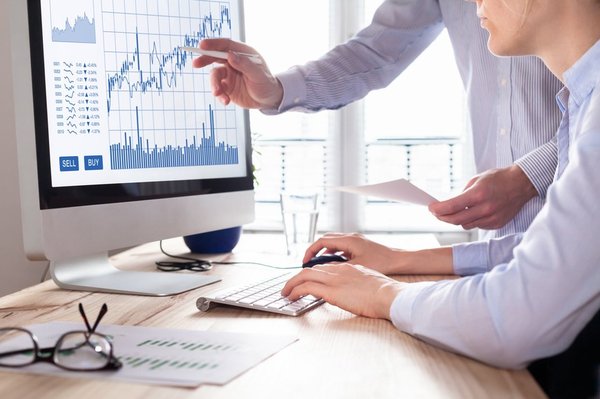 Two professional men looking at stock charts on a monitor. 