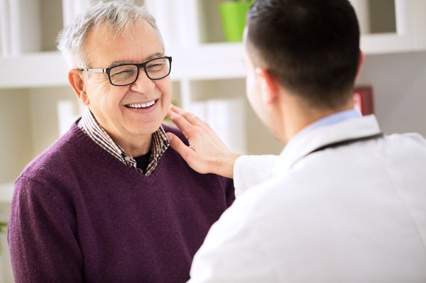 A young doctor touches an older man's shoulder.