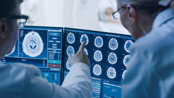 Two scientists looking at a monitor showing brain scans.