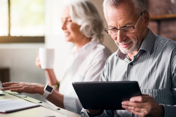 An elderly couple sitting at a table using computers.