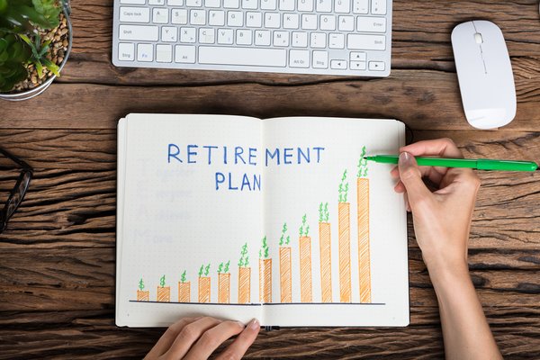 Hand holding a green pen to a paper showing a bar graph reading Retirement Plan.