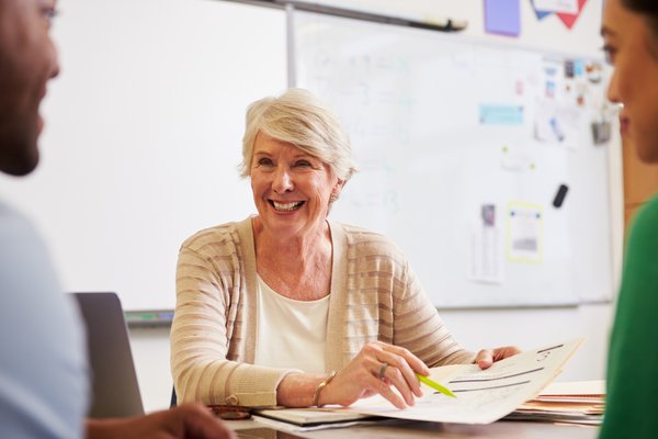 Teacher in classroom talking to students and smiling.