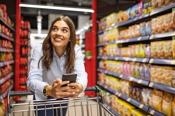 Smiling shopper pushing cart up grocery aisle.