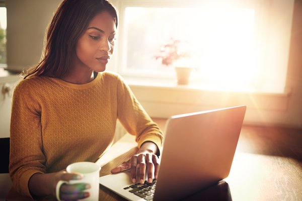 A person uses a laptop in front of a sunny window.