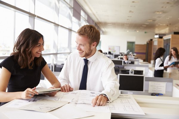 Two coworkers dressed in business attire reviewing paperwork in an open area of an office.