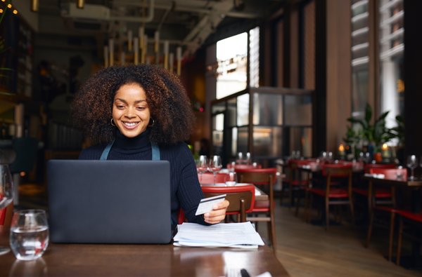 A person working in a café and holding a credit card while processing a customer's payment at a laptop.