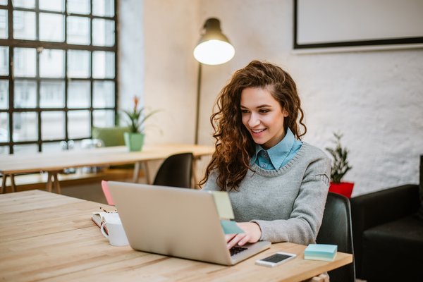 Smiling person sitting at a desk and working at a laptop.