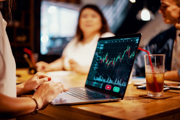 Woman sitting at table with others and looking at stock chart on laptop