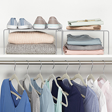 expandable metal racks holding shoes, sweaters on white shelf with clothes hanging below, white wall