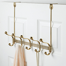 soft brass 5 hook clothing rack holding sweater and strap of purse hanging over back of white door