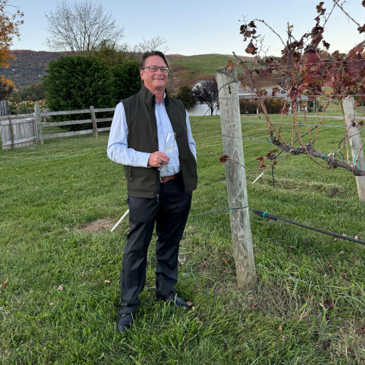 Man outside near a fence wearing a fleece vest while holding a champagne glass