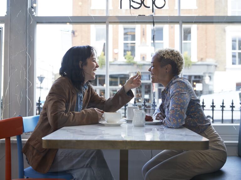 Couple enjoys coffee drinks while sitting in a bright cafe in front of a window. 