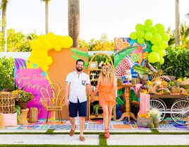 man and woman walking hand in hand in front of a bright balloon backdrop