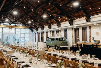 Large industrial event space with dark wood ceiling beaming, bistro lighting and a vintage mini van decor booth