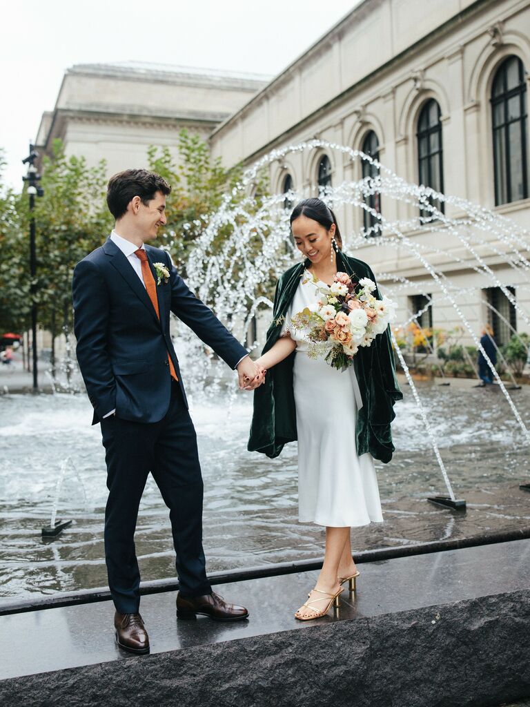 Cute Couple Poses: Couple hold hands in front of an urban fountain. 