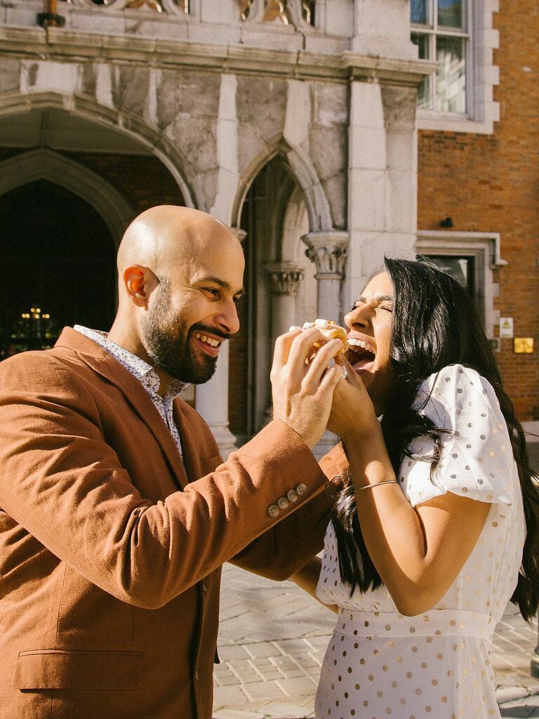 Cute Couple Poses: Couple laugh while eating donuts in the sunshine. 