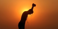 A laborer is silhouetted against the setting sun as he bathes on a hot summer day in Jammu