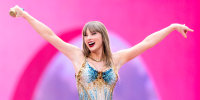 Taylor Swift performs on stage with both hands in the air