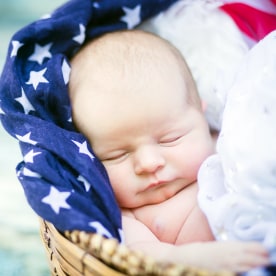 Newborn baby girl in basket surrounded by patriotic scarves.