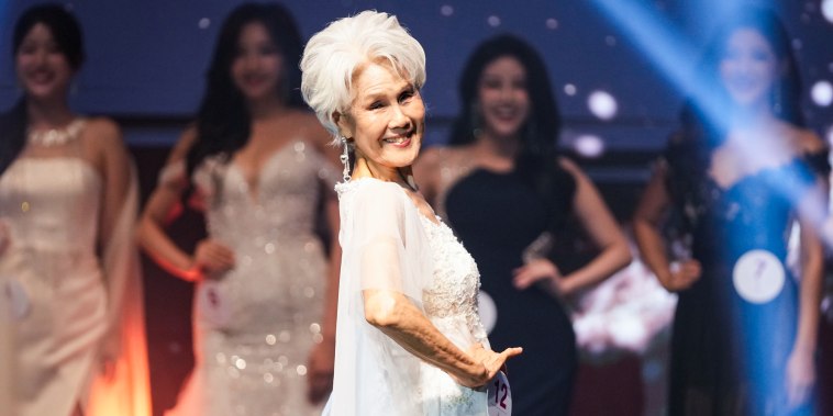 Choi Soon-hwa smiles on stage in front of other contestants, wearing a white dress