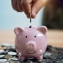 Person Putting Coin In Piggy Bank At Table