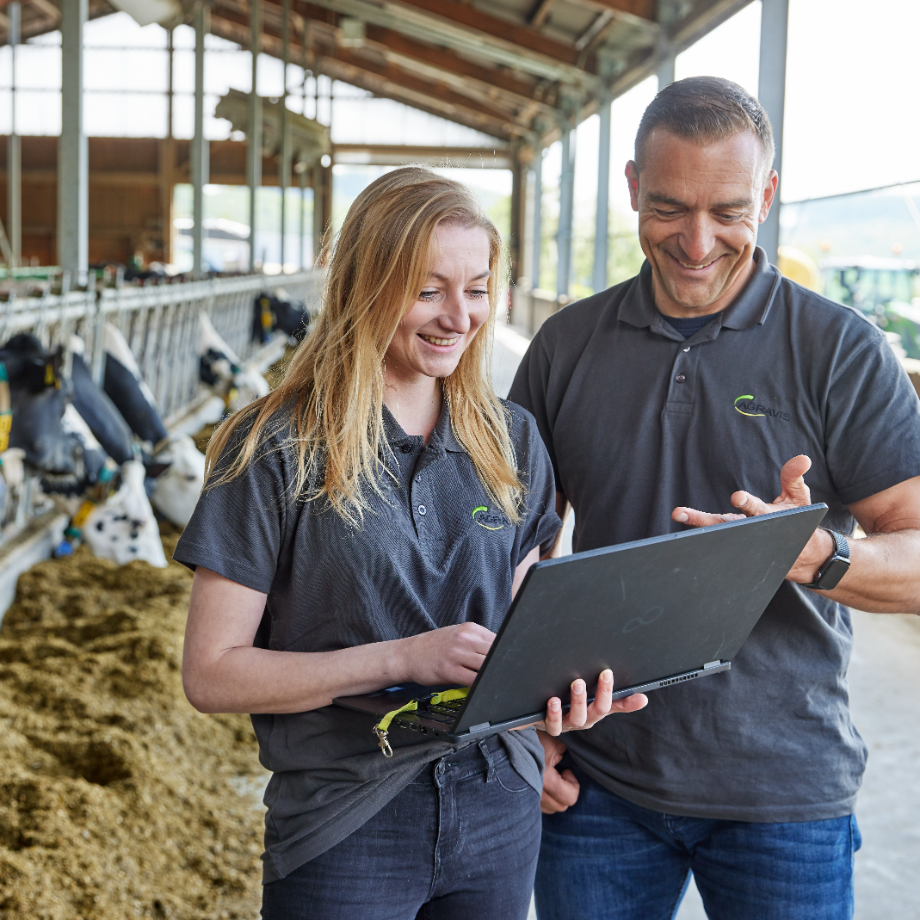 Berater vor Futtertisch im Rinderstall mit Laptop in der Hand