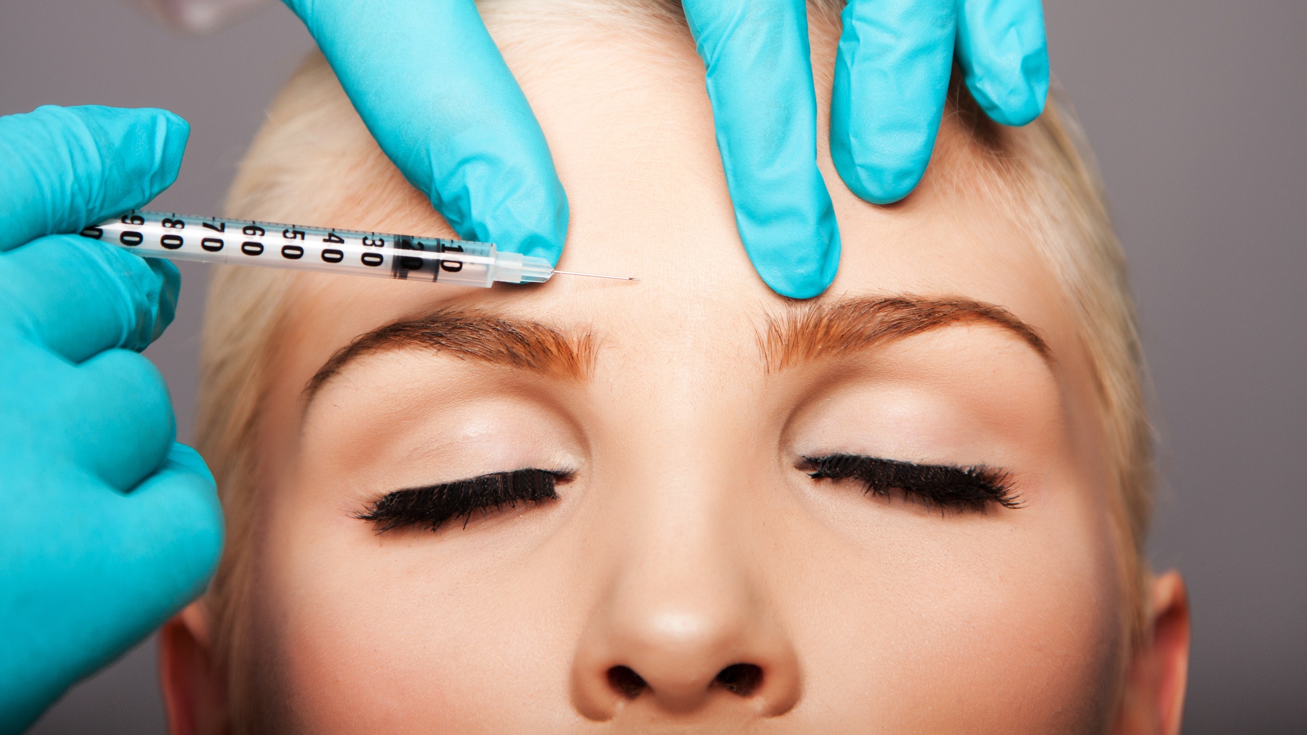 A blonde woman receives a Botox injection in her brows.